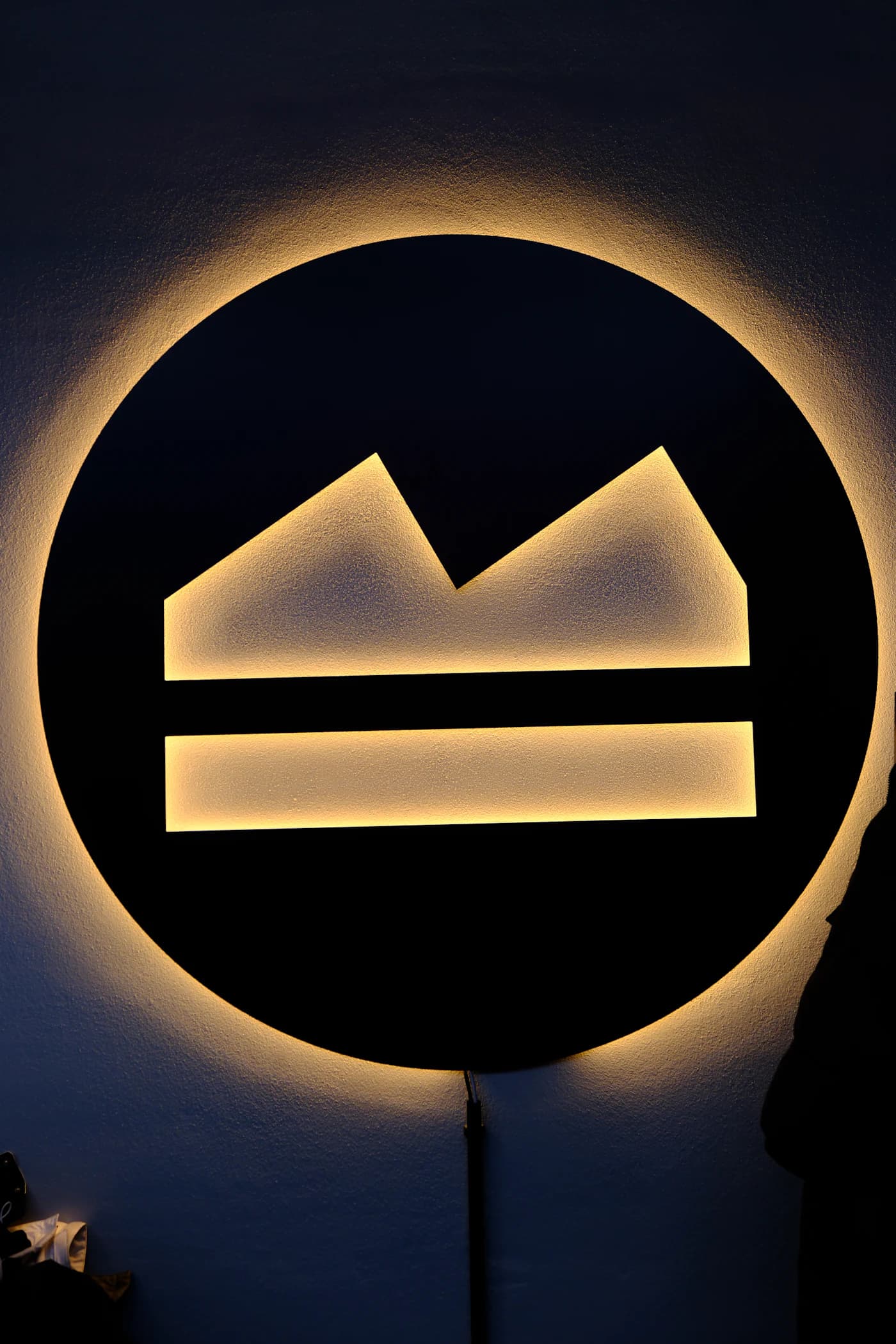 Backlit circular logo sign glowing on a dark wall